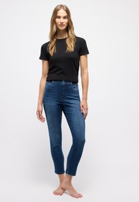 Schwarzes Kurzarm-T-Shirt kombiniert mit blauen, eng geschnittenen Jeans, die eine hohe Taille, fünf Taschen und einen leicht verjüngten Schnitt an den Knöcheln aufweisen.
