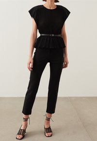 Haut péplum plissé noir à manches courtes, associé à un pantalon noir cintré et des sandales noires à lanières. Contraste textural lisse et varié.