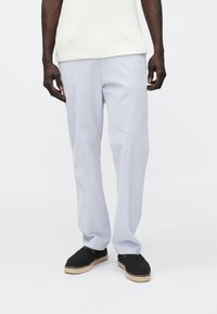 Vaaleansiniset, puuvillasekoitteesta valmistetut housut, joissa on väljä istuvuus, sivutaskut ja jotka on yhdistetty mustiin espadrillosaappaisiin. Sileä pinta.