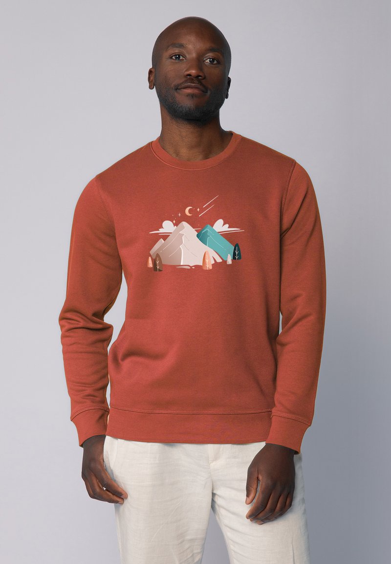 Sweatshirt en mélange de coton de couleur rouille avec un col ras du cou. Il présente un graphique frontal de montagnes et d'arbres dans des couleurs pastel. Texture douce.