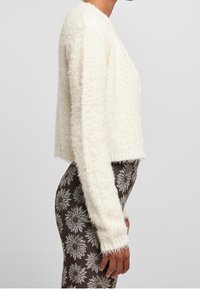 White fluffy cropped sweater with long sleeves, textured fabric, and a straight hem. Paired with brown patterned leggings featuring floral designs.
