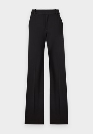 Pantalon noir taille haute, large, confectionné sur mesure, avec passants de ceinture et poches avant sur un fond clair uni.