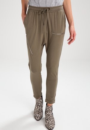 Person iført olivengrønne, tilspidsede bukser med elastisk taljebånd og lynlåslommer, kombineret med ankelstøvler med leopardprint.