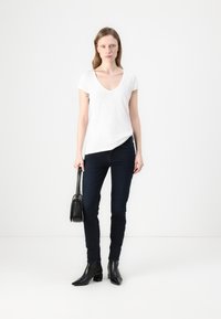 Camiseta blanca de cuello en V, jeans skinny oscuros, botas de tobillo negras con punta afilada y un pequeño bolso negro. Diseño simple y limpio, silueta ajustada.