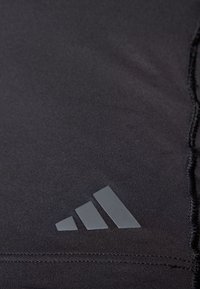 Tela atlética negra que muestra una textura suave, con un logo gris de Adidas. El diseño presenta líneas limpias y un brillo sutil.