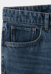 Gros plan sur un jean en denim bleu montrant la ceinture supérieure, la boucle de ceinture, les rivets et la poche avant avec une petite poche à monnaie à l'intérieur.