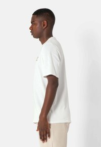 Hvid kortærmet t-shirt med rund halsudskæring, afslappet pasform og subtile bogstaver på fronten, lavet af blødt materiale.