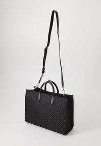 Fekete vászontáska texturált anyagból, masszív fogantyúkkal és leválasztható pánttal. Geometrikus mintázattal és sima bőrkiegészítőkkel rendelkezik.