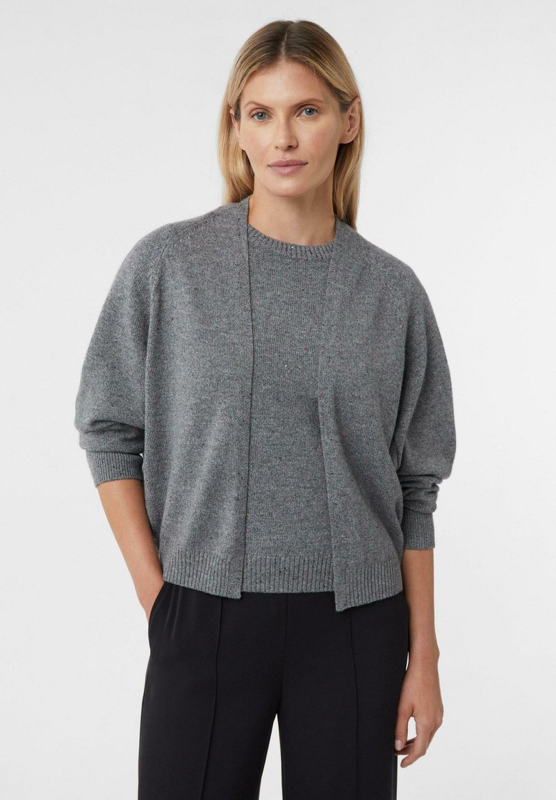 Szary sweter rozpinany na drutach z otwartym przodem, ściągaczami na mankietach i dole. Noszony na dopasowanym, szarym swetrze z okrągłym dekoltem, w połączeniu z czarnymi spodniami.