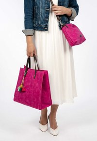 Magenta torba skórzana na ramię z brązowymi uchwytami, z plecioną teksturą i kolorowym detalem w postaci chwosta. Mała dopasowana torebka na ramię trzymana w przeciwnej ręce.
