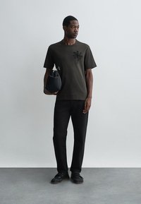 Tricou negru cu mânecă scurtă, având un broderie florală texturată pe piept, asortat cu pantaloni negri și o geantă mică neagră.