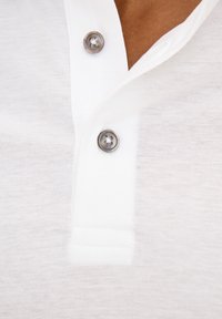 Vit polo t-shirt med en kort krage som har tre silverknappar. Tyget har en något strukturerad, lätt utseende.