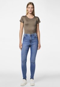 T-shirt ajusté marron à manches courtes associé à un jean bleu taille haute. Les jeans ont un design classique à cinq poches et sont fuselés au niveau de la cheville.