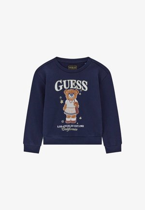 Sweat bleu marine avec un ours en jupe tenant un sac, avec le texte "GUESS" et "Los Angeles Est. 1981 California" en dessous.
