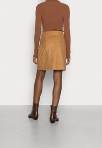 Brun ribbet langærmet top sammen med en tan ruskinds mini nederdel og brune ankelstøvler, med en tæt pasform og glat tekstur.