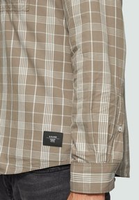 Chemise à manches courtes à carreaux beige et blanc, en coton, avec une étiquette noire, un poignet à bouton et une coupe classique.