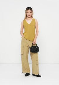 Sennepsfarvet v-hals tanktop parret med beige vidde cargo bukser med lommer og en lille, tekstureret sort håndtaske. Enkle sorte sko.