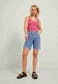 Top a righe rosa abbinato a pantaloni shorts in denim blu medio, con taglio dritto. Sandali neri con suola spessa completano l'outfit.