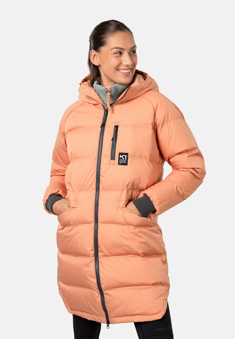 Doudoune de couleur pêche avec zip frontal, poches latérales et capuche doublée en gris. Présente une texture matelassée et un logo sur la poitrine.