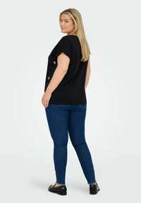 Svart kortärmad topp med avslappnad passform, som har broderade detaljer, kombinerad med blå skinny jeans och svarta skor med nitar.
