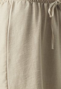 Shorts en lin beige avec une taille élastique et un cordon de serrage, présentant une texture lisse et un subtil motif de tissage diagonal.