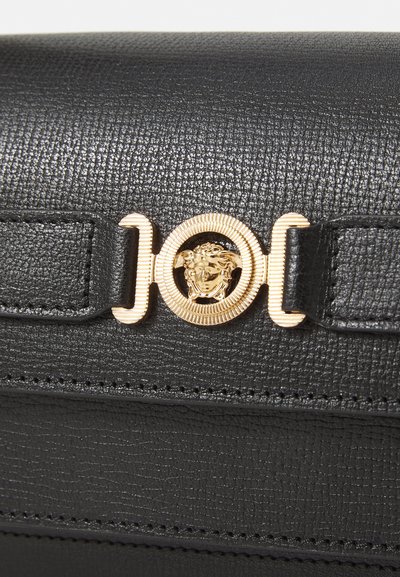 Bolso de cuero negro texturizado con un cierre de metal dorado con un diseño de cabeza de león. Costura notable a lo largo de los bordes para mayor detalle.
