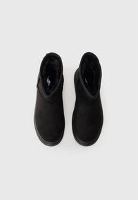 Bottines noires en matériau suédé lisse, avec un intérieur douillet, un bout arrondi et une semelle en caoutchouc plate.