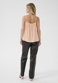 Peenevaba tipp kogutud selja detailiga, kombineeritud mustade kunstnahast pükste ja heledate plokkninaliste kingadega.