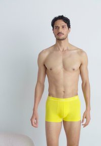 Gule bomulds boxer briefs med en tætsiddende pasform. Har et logo på taljen og en glat overflade. Båret af en model med en atletisk bygning.