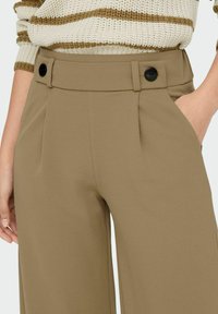 Bruine wijde broek met een op maat gemaakte uitstraling, zijzakken en zwarte knopen op de tailleband voor extra detail en structuur.