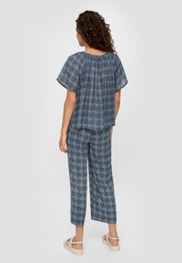 Twee-delige outfit in marineblauw met een geometrisch patroon. De bovenkant heeft een losse pasvorm en korte mouwen; de broek heeft een rechte pasvorm en is tot halverwege het scheenbeen.