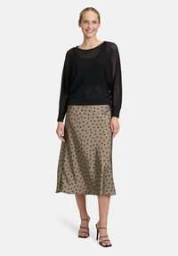 Pull en maille noir avec une coupe ample et des manches larges, associé à une jupe satin kaki longueur genoux à pois noirs. Talons hauts noirs à brides.
