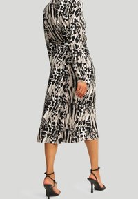Long-sleeve midi dress in a black and beige animal print. Smooth fabric with a fitted waist, flowing skirt, and side slit. Paired with black heels.
