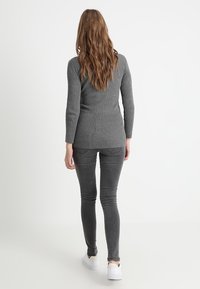 Suéter gris de canalé con mangas largas, combinado con jeans skinny de un gris oscuro. El modelo lleva zapatillas blancas, mostrando un atuendo casual desde detrás.