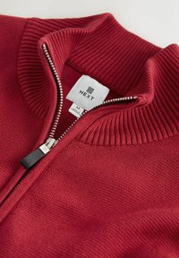 Burgundy zip-up sweater with ribbed collar. Features a silver zipper and a label reading "NEXT" with size tag "M." Smooth texture.
