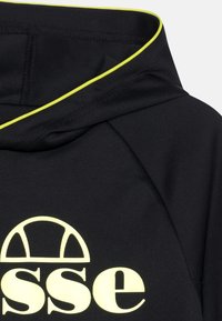 Czarna bluza z kapturem z żółtymi akcentami wzdłuż kołnierza. Z przodu widnieje okrągły projekt logo w kolorze żółtym. Gładki, elastyczny materiał.