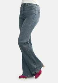 Jeans de mezclilla azul acampanados con un diseño de cinco bolsillos y costuras en contraste; combinados con zapatos de tacón rosa que presentan una punta redonda.