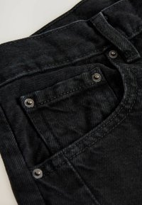 Jeans in denim nero con tasca frontale con rivetti metallici e superficie in tessuto testurizzato. Dettagli cuciti lungo la vita e le cuciture.