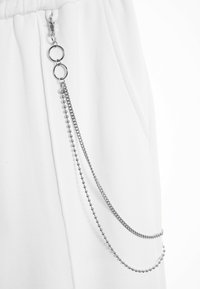 Tela blanca con un detalle de cadena plateada, que presenta dos bucles y dos tipos de cadenas: una cadena de bolas y una cadena plana de eslabones.