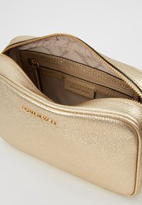 Bolso de mano texturizado en dorado con cierre de cremallera, que cuenta con un interior suave y un pequeño bolsillo con cremallera para la organización.