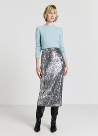 Hellblauer, gestrickter Pullover mit langen Ärmeln, kombiniert mit einem silbernen Pailletten-Midi-Rock. Das Modell trägt schwarze kniehohe Stiefel.