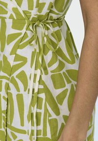 Robe à motifs verts et blancs en tissu léger, avec une taille nouée et des formes abstraites. Accent sur la texture lisse et le design décontracté.
