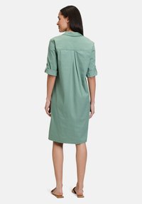 Mintgrünes Kleid mit kurzen Ärmeln, mit einem Kragen, aufgerollten Manschetten und einem Rückenfalte für zusätzliche Struktur. Glattes, leichtes Material.