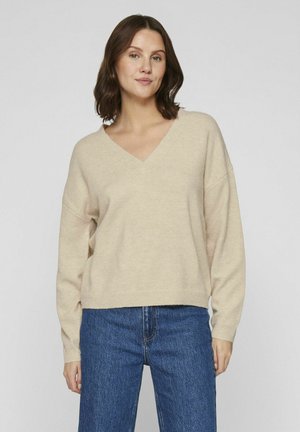 Beige v-neck sweater with long sleeves, relaxed fit, and ribbed hem, paired with blue denim jeans. Soft texture; minimal design.