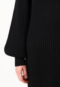 Black knitted dress with a ribbed texture, featuring long, voluminous sleeves and a fitted silhouette, focusing on warmth and comfort.