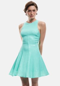 Un vestito aderente senza maniche di un luminoso verde menta con gonna svasata, caratterizzato da un tessuto testurizzato e sottili dettagli di paillettes.
