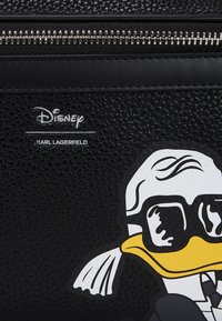 Pochette in pelle nera texture con zip argentata, caratterizzata da un vivace design di Paperino e i marchi: "Disney" e "Karl Lagerfeld."