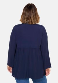 Marinblå, långärmad tröja med avslappnad passform, plisserad baksida och rund halsringning. Slät tygtextur utan synliga mönster.