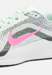 Buty sportowe Nike z białą i czarną dzianinową cholewką, różowym logo, miętowozielonymi akcentami oraz teksturowaną szarą podeszwą. Posiadają zapięcie na sznurowadła i przewiewny design.