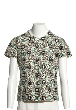 Haut beige à manches courtes avec motifs circulaires et floraux noirs et accents turquoise sur un torse de mannequin blanc, sans tête ni mains.
